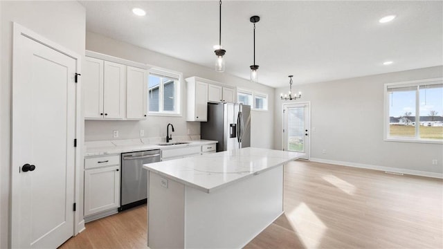 kitchen featuring white cabinetry, a center island, sink, stainless steel appliances, and decorative light fixtures