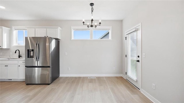 kitchen featuring sink, white cabinetry, stainless steel refrigerator with ice dispenser, and hanging light fixtures