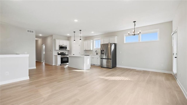 kitchen featuring white cabinets, a center island, stainless steel appliances, and hanging light fixtures