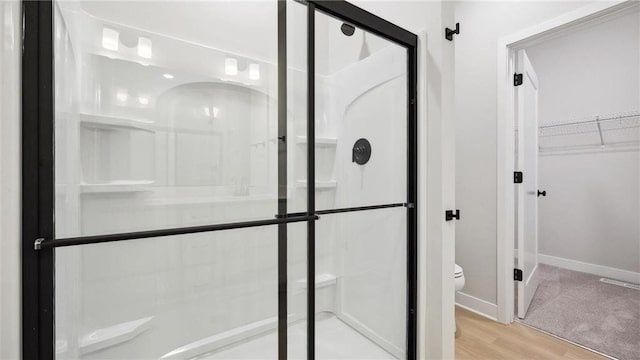 bathroom with hardwood / wood-style floors, toilet, and a shower with door