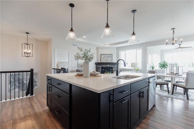 kitchen with a center island with sink, a raised ceiling, sink, hanging light fixtures, and a fireplace