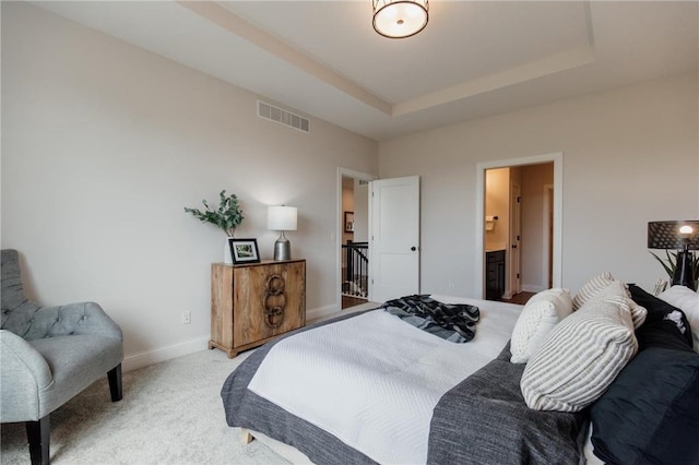 bedroom featuring carpet, ensuite bathroom, and a tray ceiling