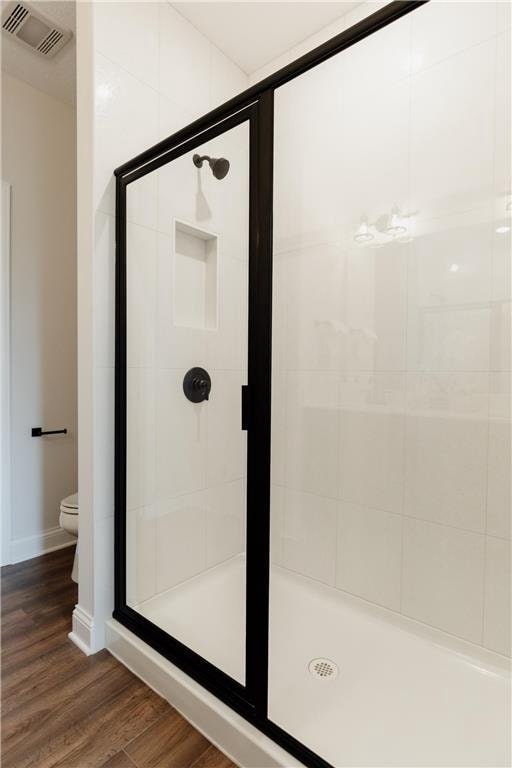 bathroom with hardwood / wood-style floors, toilet, and a shower with shower door