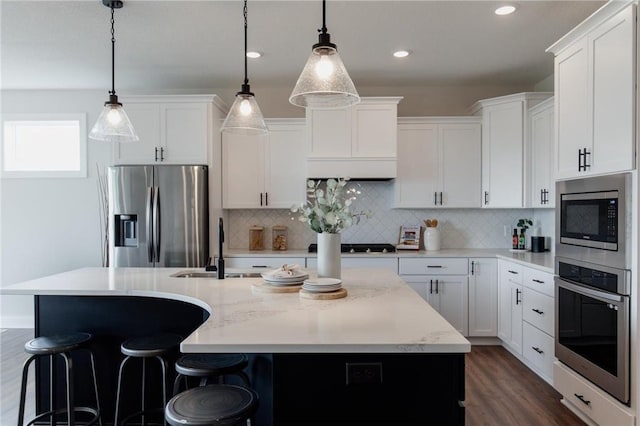 kitchen featuring white cabinets, appliances with stainless steel finishes, decorative light fixtures, and an island with sink