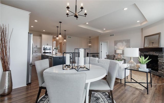 dining room with dark hardwood / wood-style flooring, a tray ceiling, sink, an inviting chandelier, and a stone fireplace