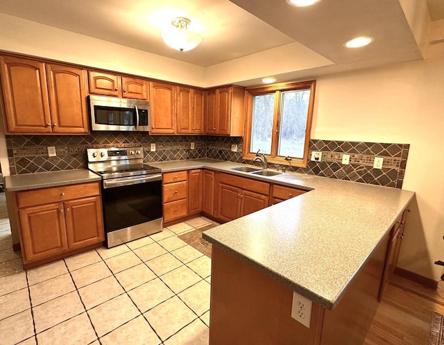 kitchen with backsplash, kitchen peninsula, sink, and appliances with stainless steel finishes