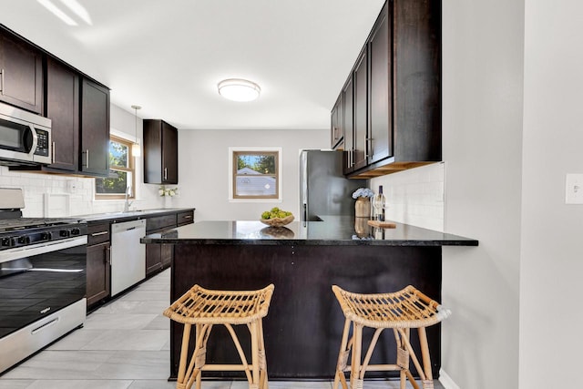 kitchen featuring stainless steel appliances, a kitchen breakfast bar, tasteful backsplash, kitchen peninsula, and dark brown cabinets