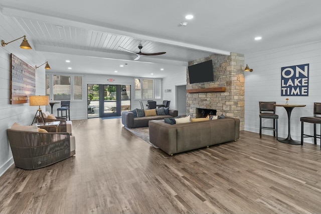 living room with ceiling fan, wooden walls, beam ceiling, a fireplace, and hardwood / wood-style floors