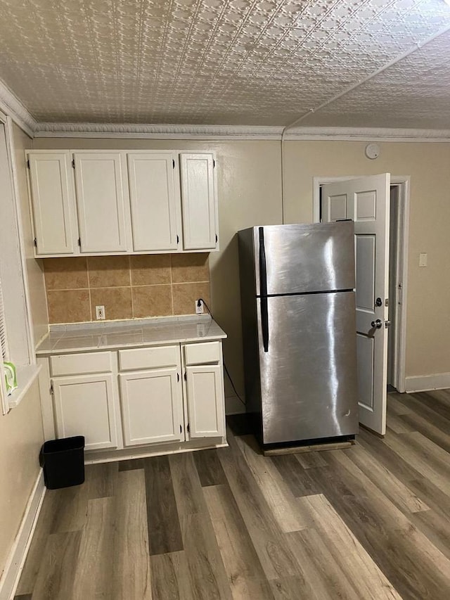 kitchen featuring stainless steel refrigerator, white cabinetry, dark hardwood / wood-style floors, backsplash, and ornamental molding