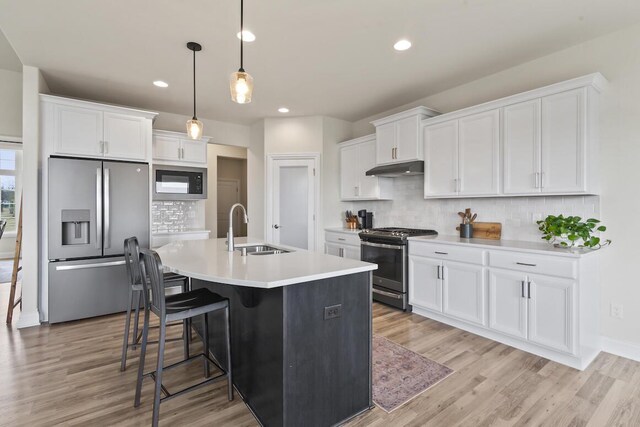 kitchen with stainless steel appliances, sink, pendant lighting, white cabinets, and an island with sink