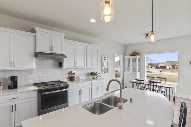 kitchen featuring backsplash, stainless steel range, sink, white cabinets, and hanging light fixtures