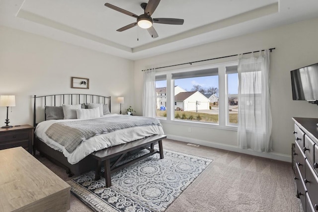 carpeted bedroom with a raised ceiling and ceiling fan