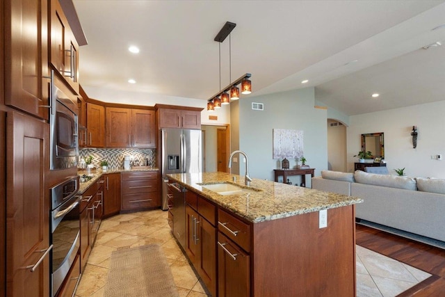 kitchen with appliances with stainless steel finishes, light stone counters, vaulted ceiling, sink, and a center island with sink