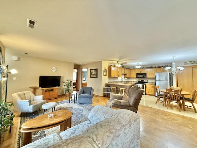 living room with ceiling fan with notable chandelier, light hardwood / wood-style floors, and sink