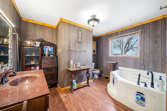 bathroom with a washtub, wood walls, toilet, vanity, and ornamental molding