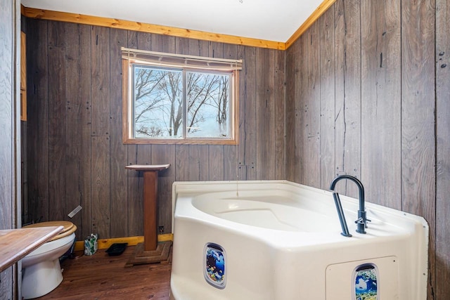 bathroom featuring toilet, wood-type flooring, a tub, and wooden walls