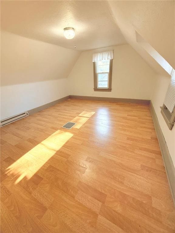 additional living space featuring baseboard heating, light hardwood / wood-style floors, and vaulted ceiling