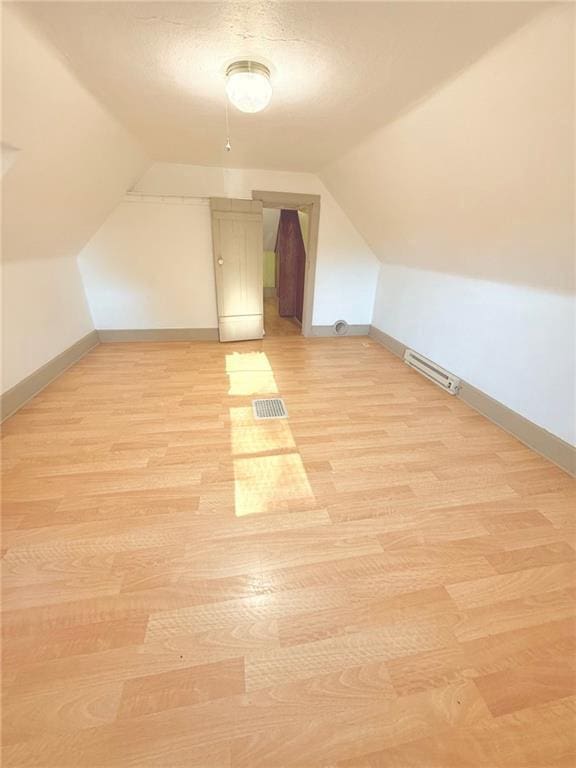 additional living space with light wood-type flooring, a textured ceiling, and vaulted ceiling