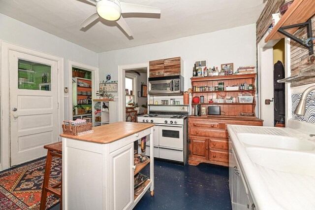 kitchen featuring ceiling fan, sink, white cabinets, a kitchen island, and white gas stove