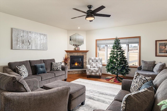 living room with ceiling fan, a stone fireplace, and light hardwood / wood-style flooring