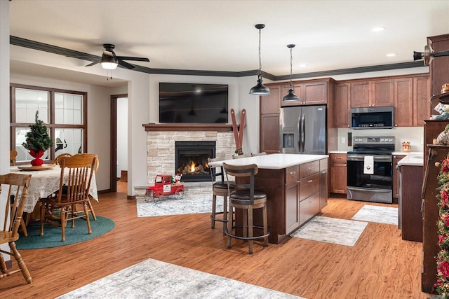 kitchen with light wood-type flooring, stainless steel appliances, ceiling fan, pendant lighting, and a fireplace