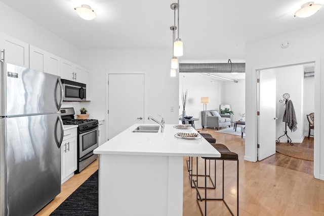 kitchen featuring pendant lighting, a center island with sink, white cabinets, sink, and stainless steel appliances