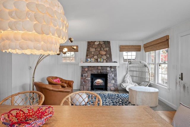 dining room featuring hardwood / wood-style flooring, a stone fireplace, and wooden walls