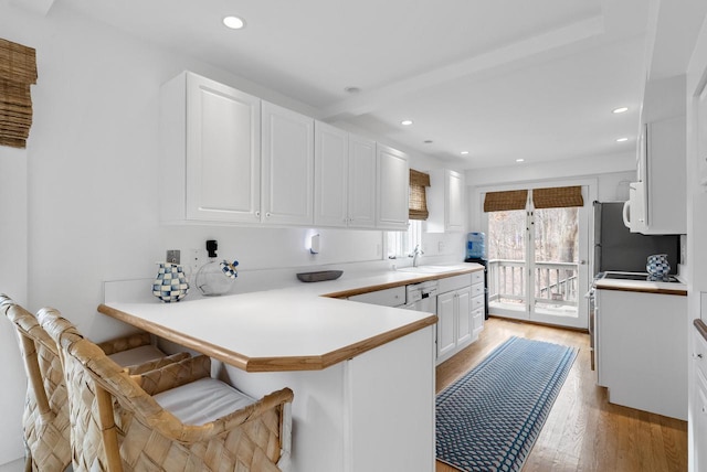 kitchen with kitchen peninsula, a breakfast bar, sink, white cabinets, and light hardwood / wood-style floors