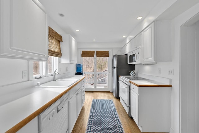 kitchen with white cabinetry, white appliances, sink, and light hardwood / wood-style flooring