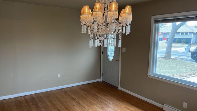 foyer entrance with wood-type flooring, a baseboard radiator, and an inviting chandelier