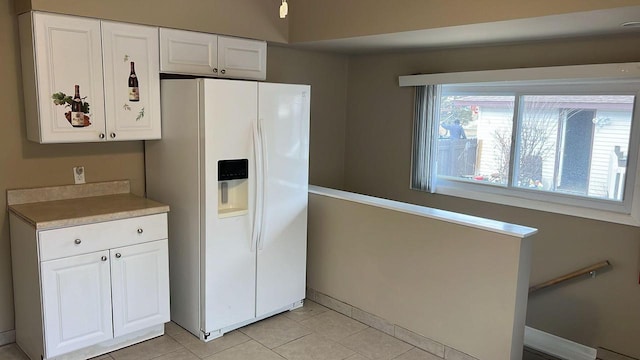 kitchen featuring white fridge with ice dispenser, white cabinets, and light tile patterned flooring