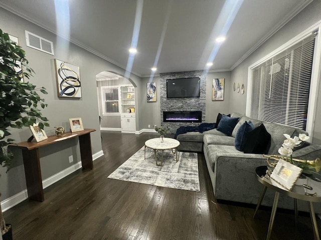 living room with a stone fireplace, built in features, dark hardwood / wood-style floors, and ornamental molding