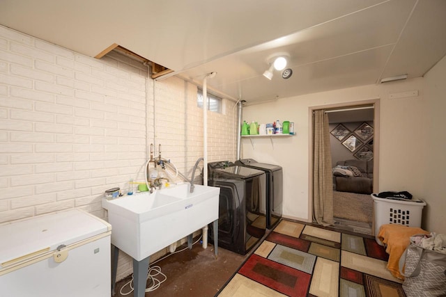 laundry room with independent washer and dryer, sink, and brick wall