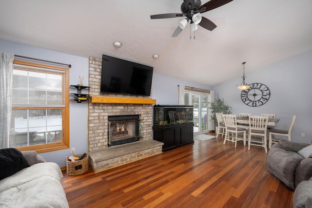 living room with ceiling fan, hardwood / wood-style floors, vaulted ceiling, and a brick fireplace