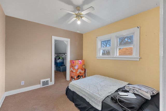 carpeted bedroom with a walk in closet and ceiling fan