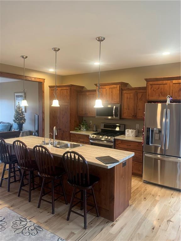 kitchen with appliances with stainless steel finishes, a breakfast bar, sink, pendant lighting, and light hardwood / wood-style floors