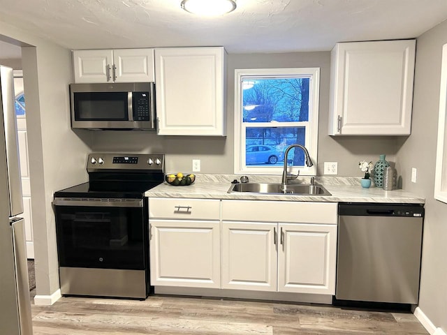 kitchen featuring white cabinetry, sink, stainless steel appliances, and light hardwood / wood-style floors