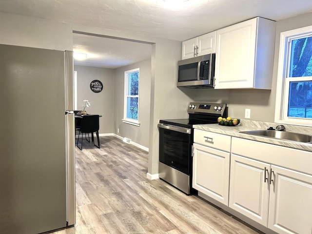 kitchen featuring appliances with stainless steel finishes, light hardwood / wood-style floors, white cabinetry, and sink