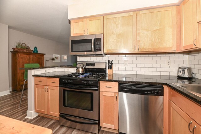 kitchen featuring light brown cabinets, backsplash, dark wood-type flooring, kitchen peninsula, and stainless steel appliances