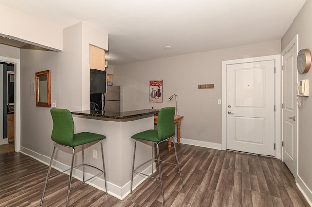 kitchen with a kitchen bar, kitchen peninsula, stainless steel refrigerator, and dark wood-type flooring