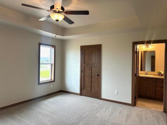 unfurnished bedroom with light carpet, ensuite bath, a raised ceiling, and ceiling fan