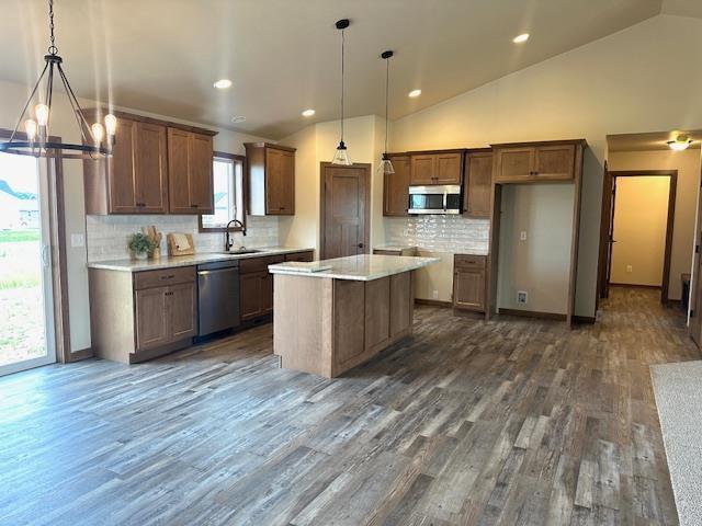 kitchen featuring pendant lighting, an inviting chandelier, dark hardwood / wood-style floors, a kitchen island, and stainless steel appliances