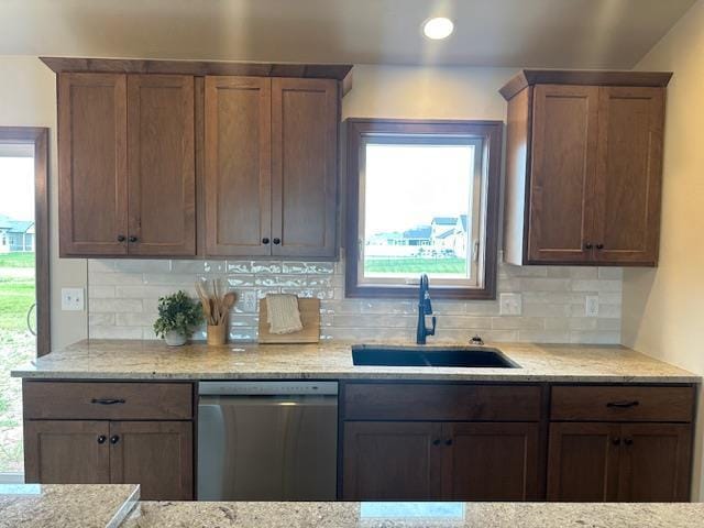 kitchen featuring stainless steel dishwasher, plenty of natural light, light stone counters, and sink