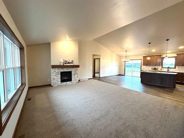 unfurnished living room featuring a fireplace, dark hardwood / wood-style floors, vaulted ceiling, and a notable chandelier