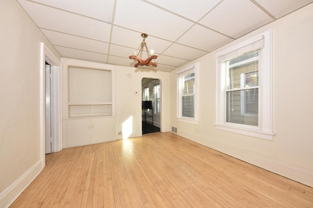 unfurnished room featuring light wood-type flooring, a drop ceiling, and a notable chandelier