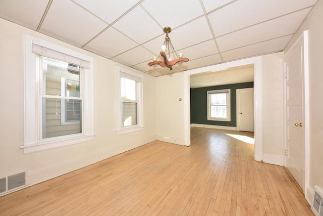 unfurnished room with a drop ceiling, a chandelier, plenty of natural light, and light wood-type flooring