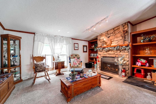 living room with a textured ceiling, track lighting, a stone fireplace, and light colored carpet