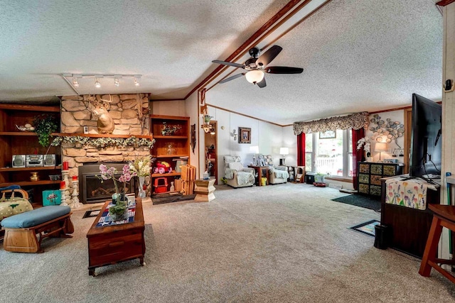 carpeted living room featuring ceiling fan, rail lighting, a stone fireplace, crown molding, and a textured ceiling