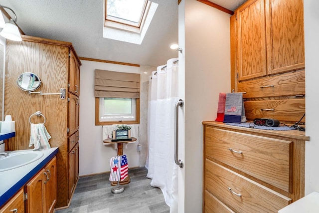 bathroom featuring a skylight, ornamental molding, a textured ceiling, vanity, and hardwood / wood-style flooring