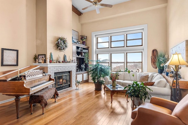 living room with ceiling fan, a towering ceiling, light hardwood / wood-style floors, and a brick fireplace